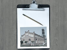 Klemmbrett mit Bleistift und Bild des Fördergerüstes Asse 2 auf einer Holzunterlage