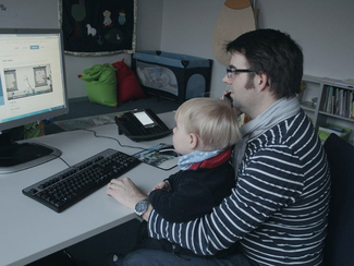 Vater arbeitet mit Kind auf dem Schoß am PC