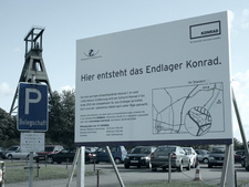Das Bild zeigt das neue Schild an der Schachtanlage Konrad 1 mit dem alten Förderturm im Hintergrund