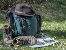 Wanderrucksack mit Hut und Wanderstiefel neben Wanderkarte und Kompass auf einer Wiese Wanderrucksack mit Hut und Wanderstiefel neben Wanderkarte und Kompass auf einer Wiese